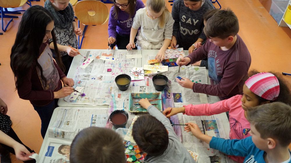 Schüler stehen um Tisch beim Malen