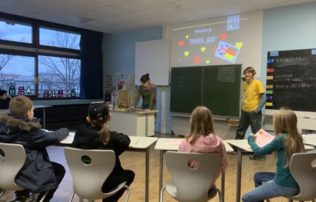 Zwei Lehrerinnen vor einer Gruppe Schüler mit Tafel und Beamerbild bei thrs-go!